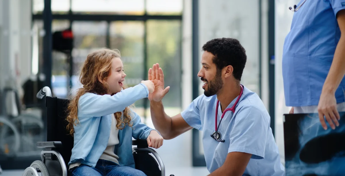Physician high-fiving a young patient in a wheelchair, the kind of patient relationships that help rural healthcare attract and keep providers