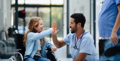 Physician high-fiving a young patient in a wheelchair, the kind of patient relationships that help rural healthcare attract and keep providers