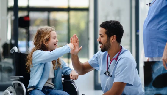 Physician high-fiving a young patient in a wheelchair, the kind of patient relationships that help rural healthcare attract and keep providers