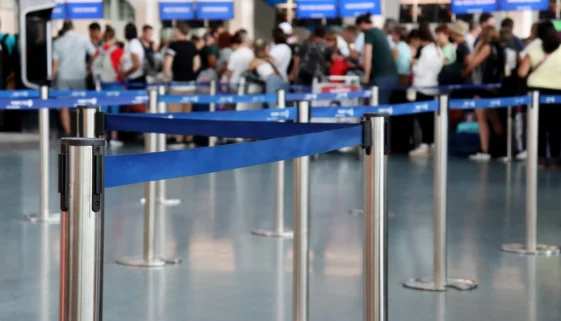 Travelers wait in a roped queue at an airport check-in area, the kind of friction government CX projects aim to reduce