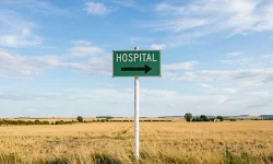 A green HOSPITAL road sign with a directional arrow stands in an open field of farmland, the kind of rural community where provider vacancies and a long time-to-hire hit hardest