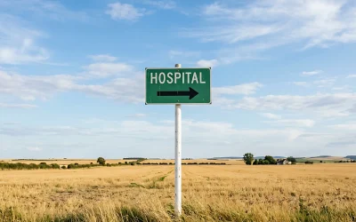 A green HOSPITAL road sign with a directional arrow stands in an open field of farmland, the kind of rural community where provider vacancies and a long time-to-hire hit hardest